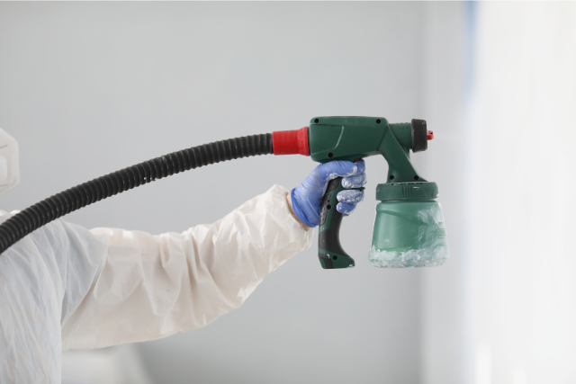 Worker painting a wall white with a paint sprayer