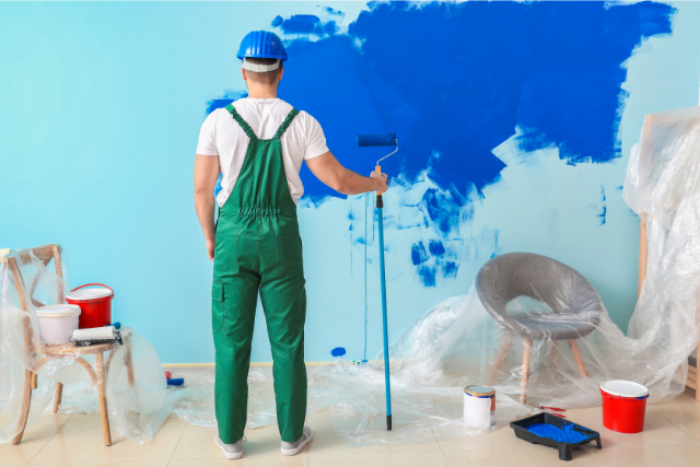 Worker looking at painting a wall blue.